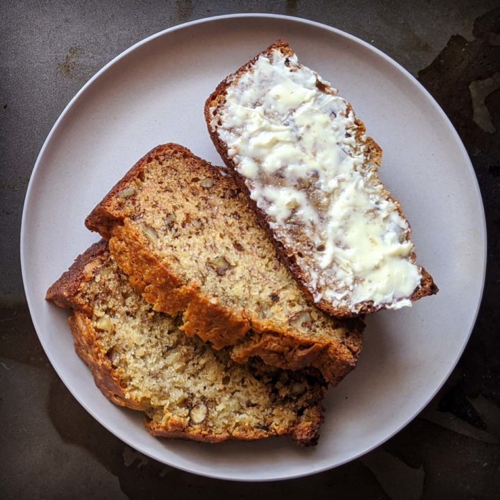 Old fashioned banana bread on a tray, one slice is buttered