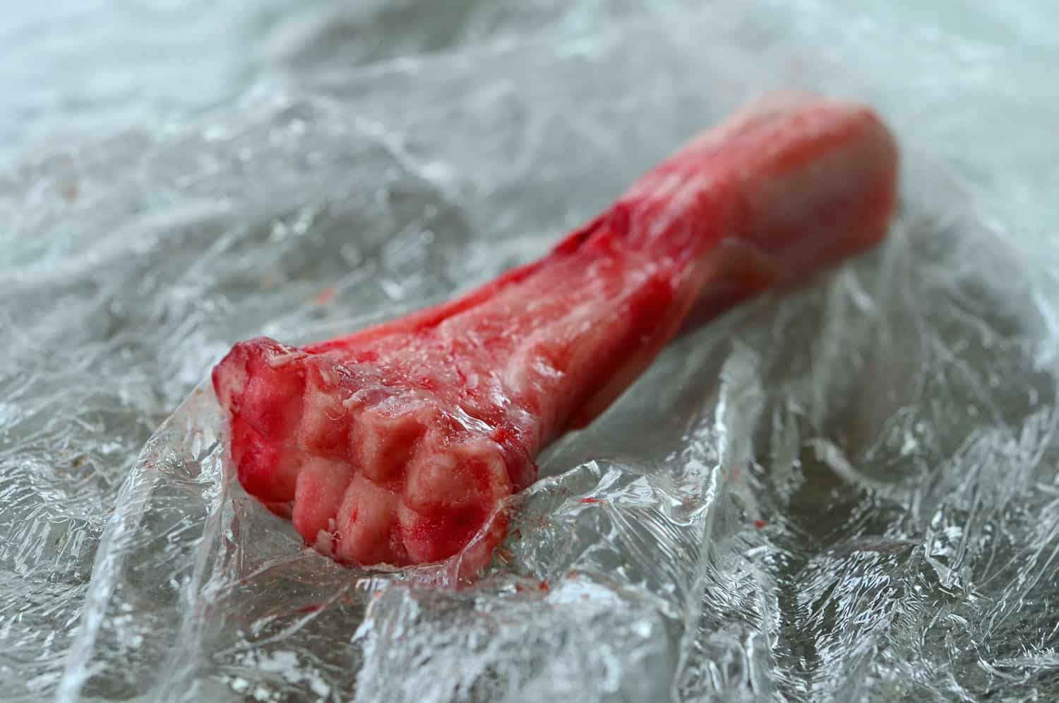 Unroasted lamb bone on plastic wrap.