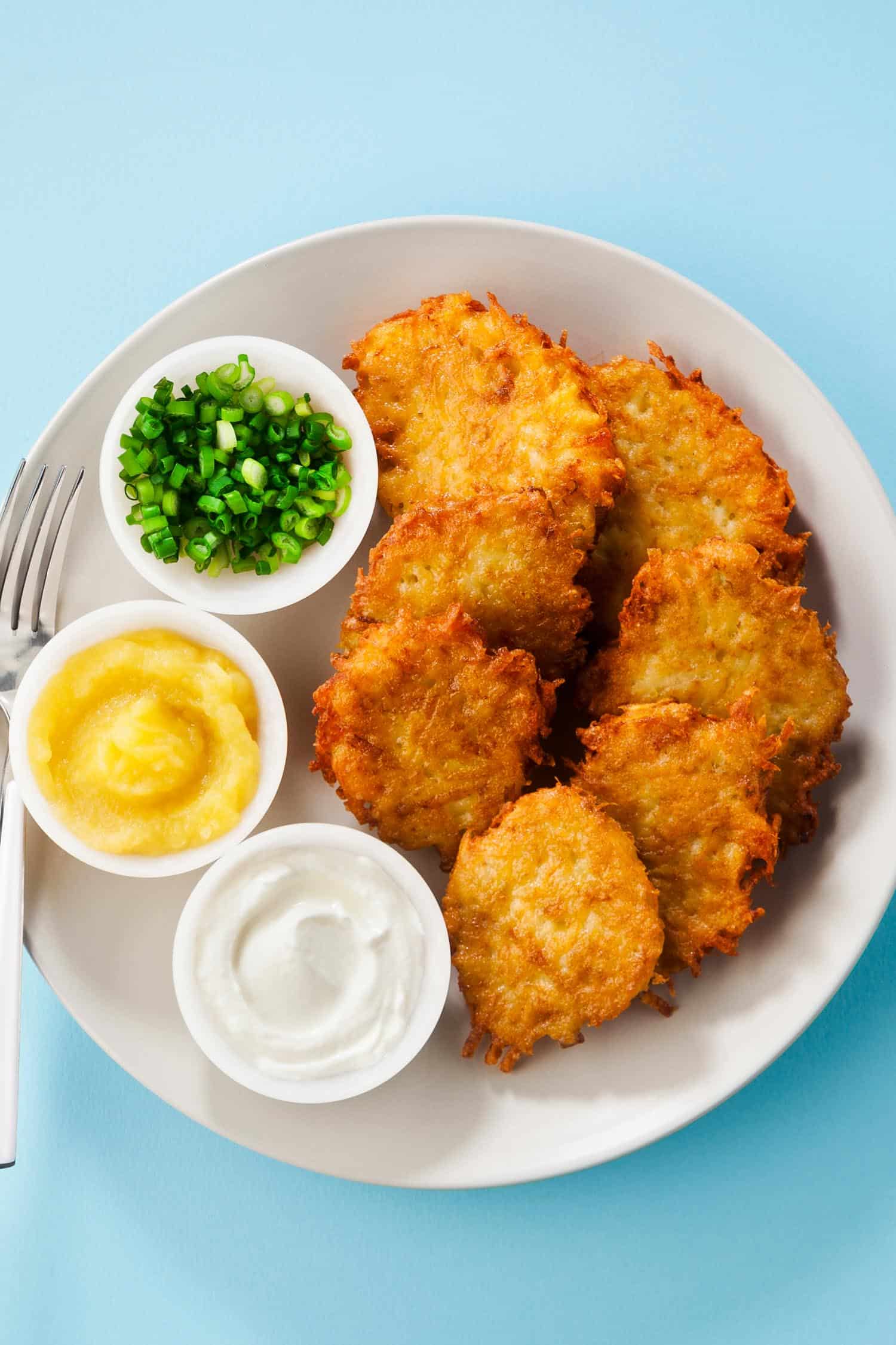 Potato pancakes, latkes or boxty and sauces from sour cream, yogurt, apple sauce and finely chopped green onion isolated on a blue background