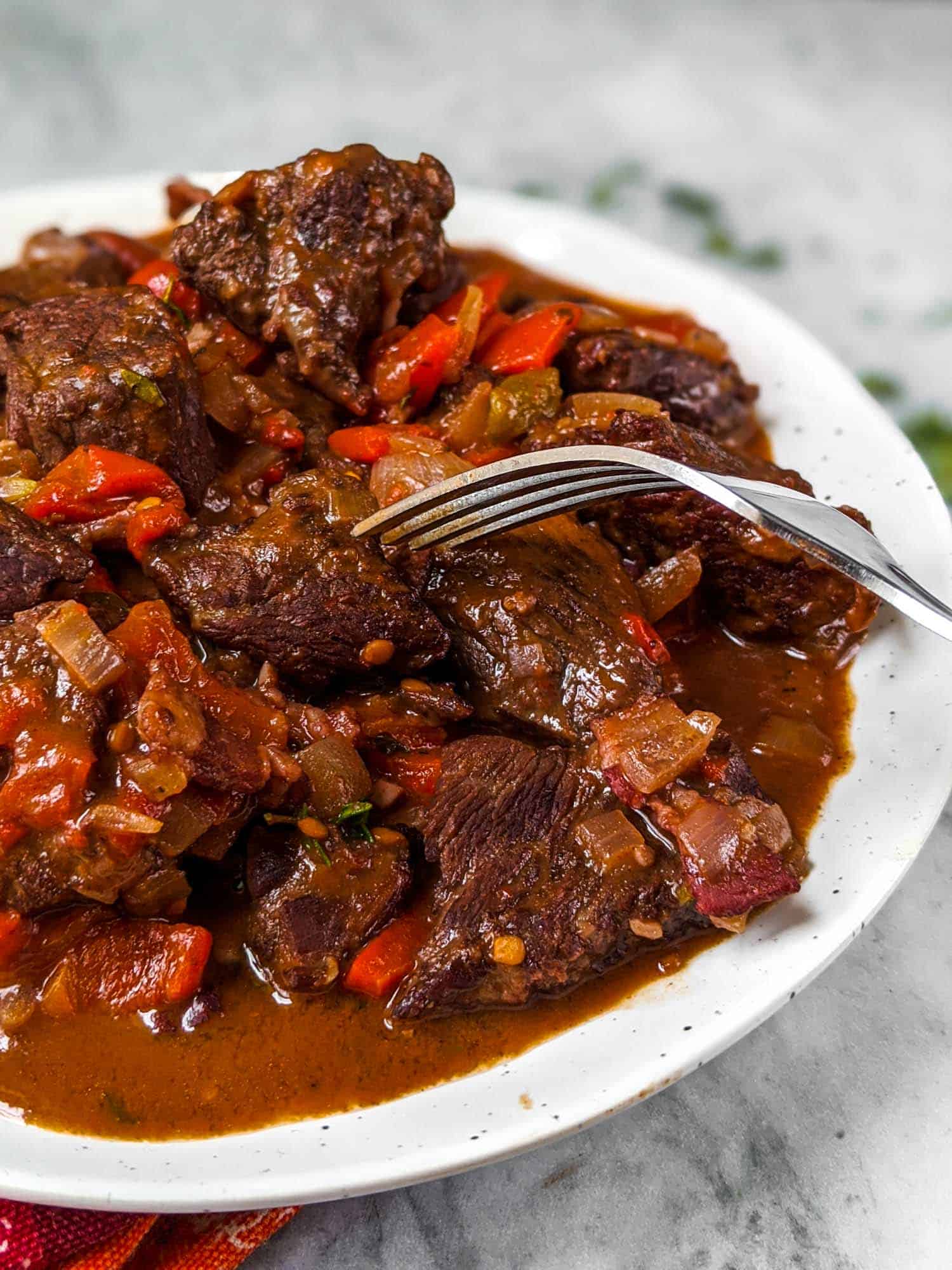Spanish beef stew with roasted red peppers on a white plate with a fork.