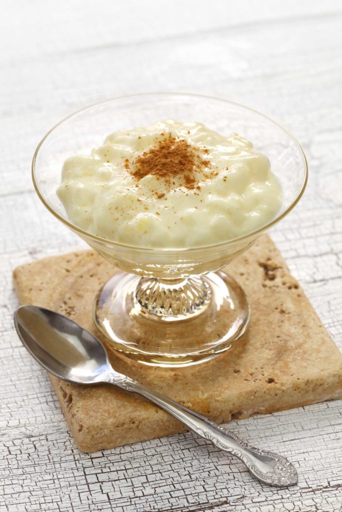 Honduran dessert arroz con leche in a clear glass bowl with a spoon on a white table.