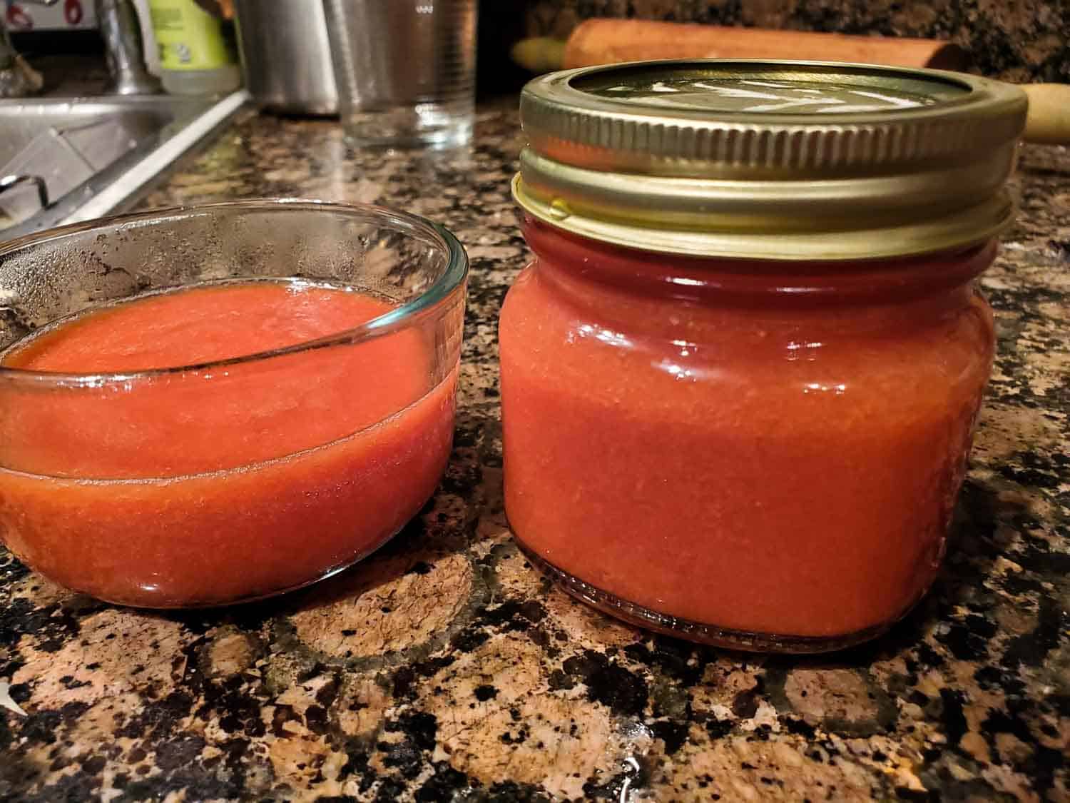 Guava jam in a preserving jar along side a clear bowl of it on a kitchen counter