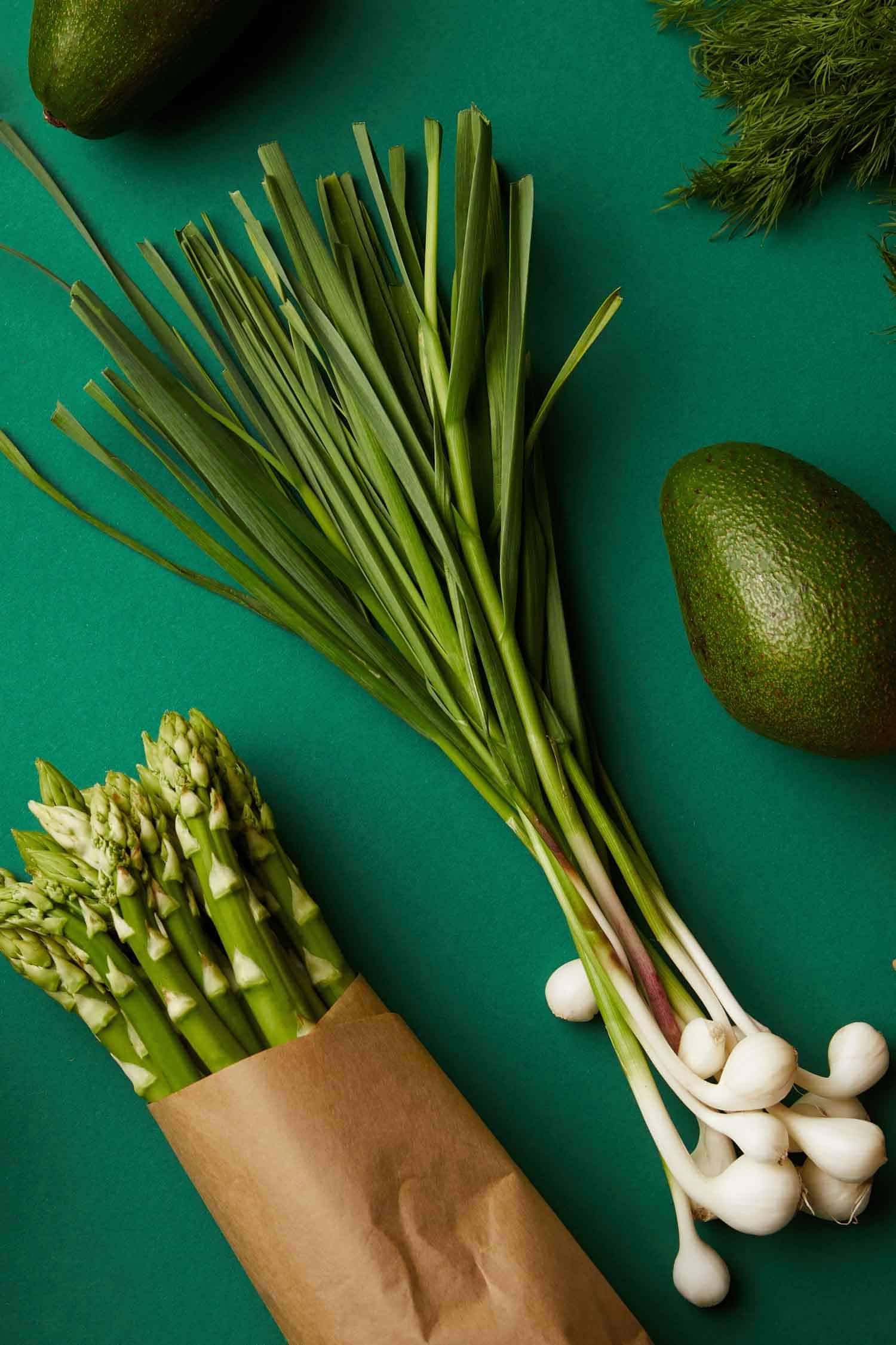 Green garlic on a green background alongside asparagus and avocado