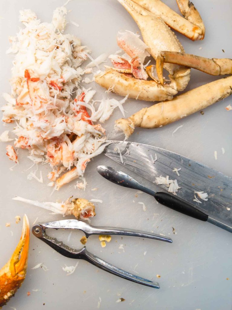 snow crab claws and meat on a white cutting board with a knife and cracker