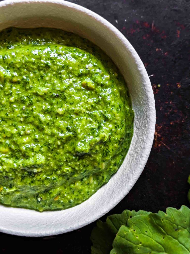 Close up of radish leaf pesto in white bowl with dark background