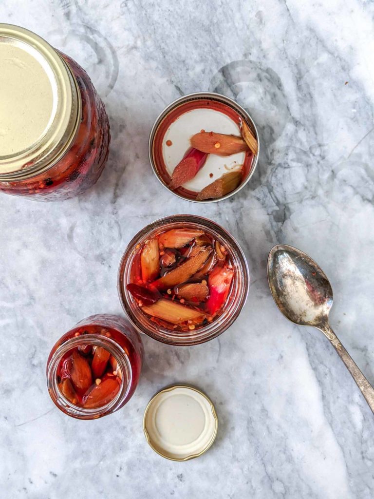 Top view of three jars of spicy pickled rhubarb with a spoon