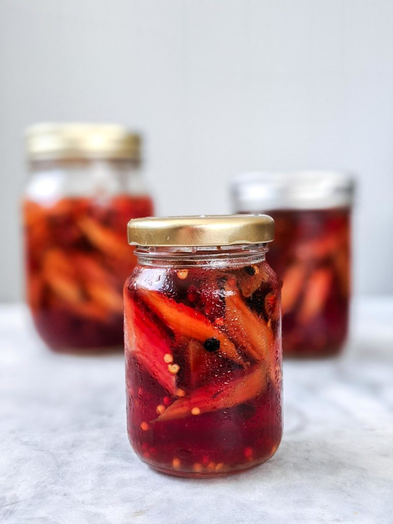 Three jars of rhubarb pickles, one in focus on marble countertop