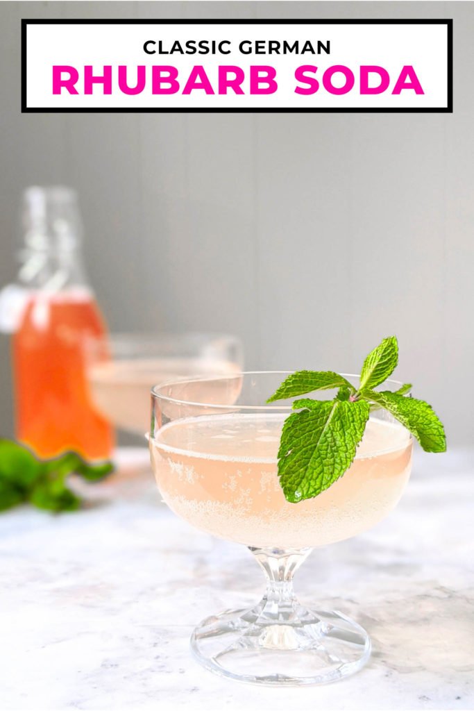 Rhubarb soda called rhabarberschorle in two coupe glasses with syrup bottle in background.