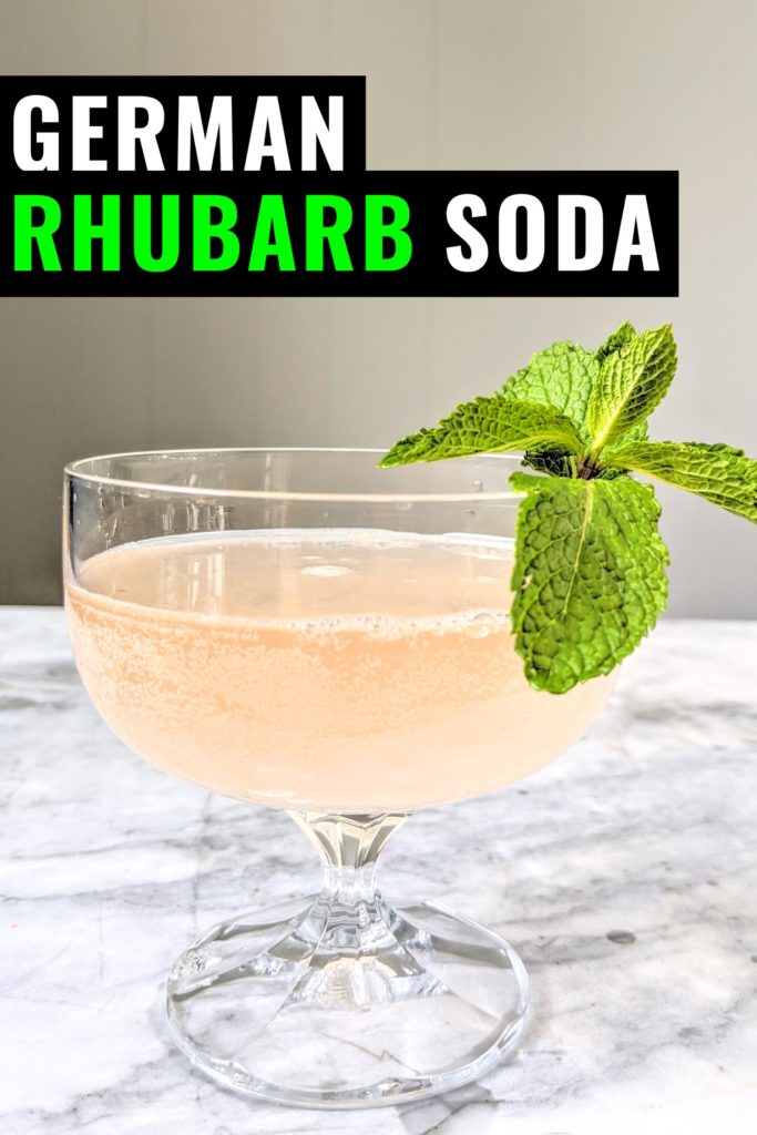 Rhubarb soda called rhabarberschorle in a coupe glass garnished with mint, on a marble background