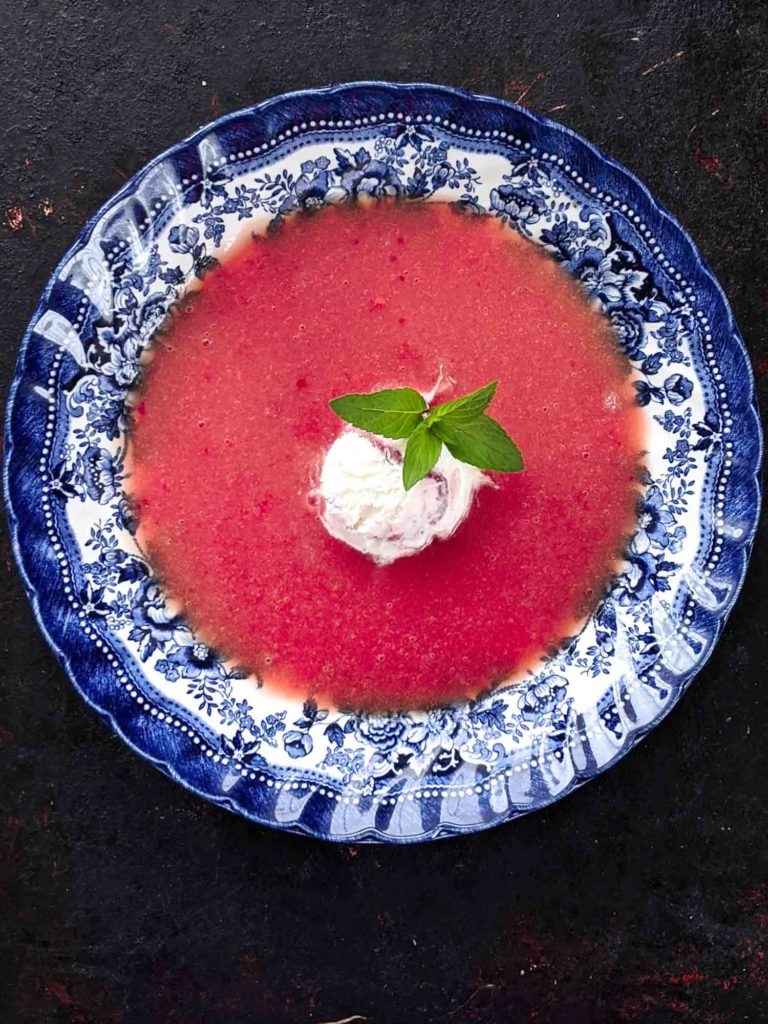 cold rhubarb soup on a black background in an antique bowl garnished with ice cream and mint