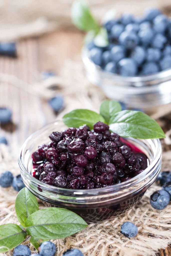 Portion of canned Blueberries on wooden background (close-up shot)