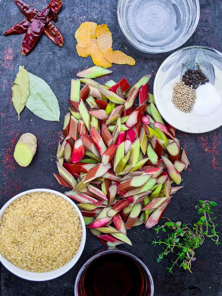 Ingredients for spicy pickled rhubarb on a baking sheet including turbinado sugar, ginger, bay leaves, dried chili peppers, orange peel, pepper, mustard seeds, sea salt, fresh type and red wine vinegar