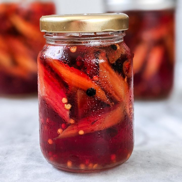 Pickled rhubarb vinegar in a jar on a white marble top with two more jars out of focus in background.