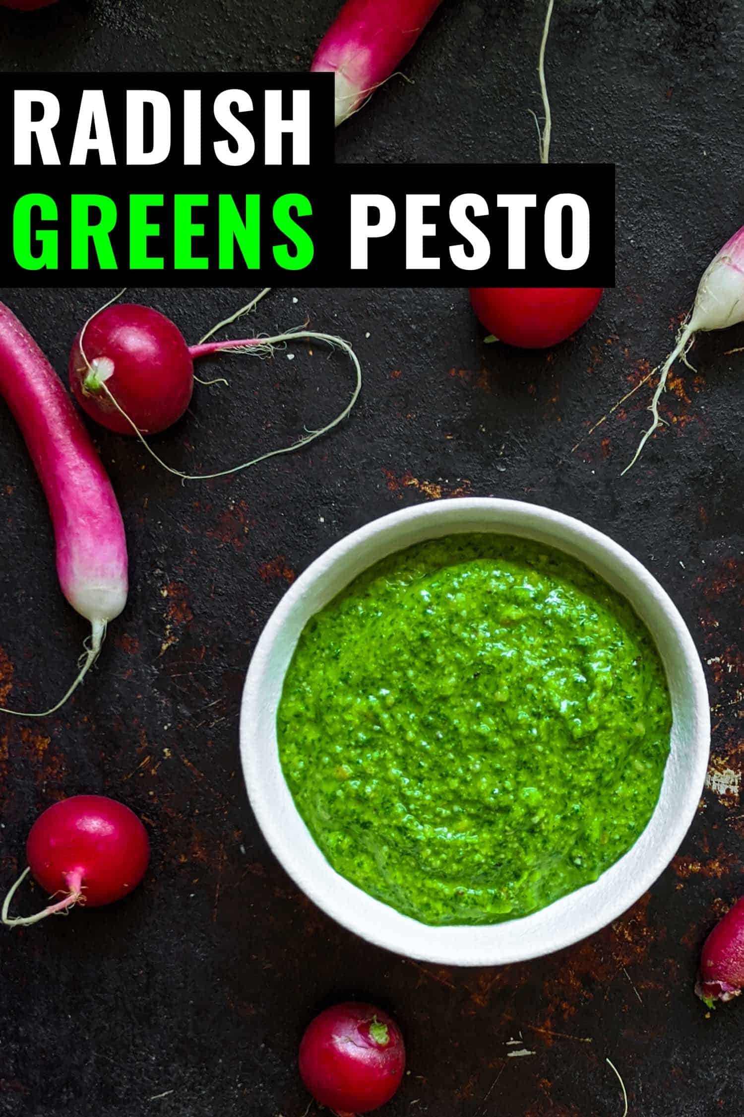 Radish top pesto on a dark background surrounded by two kinds of radishes and leaves