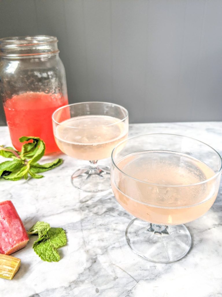 Rhubarb soda called rhabarberschorle in two coupe glasses with syrup bottle in background.