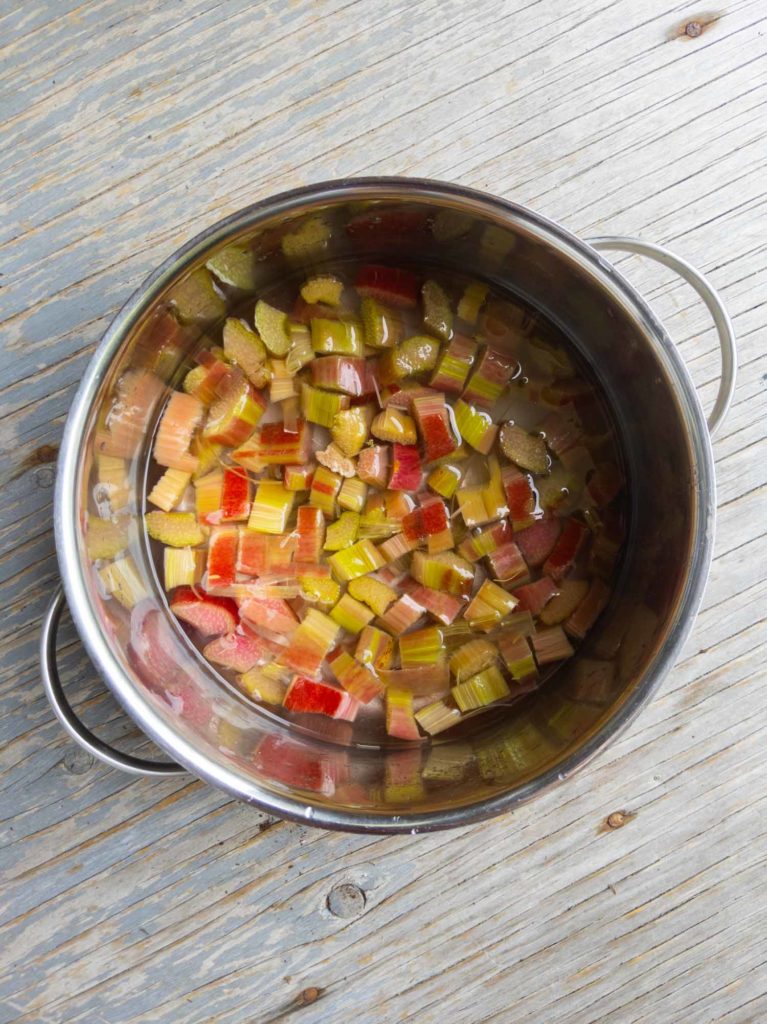 chopped rhubarb in a pot with water on a wooden background