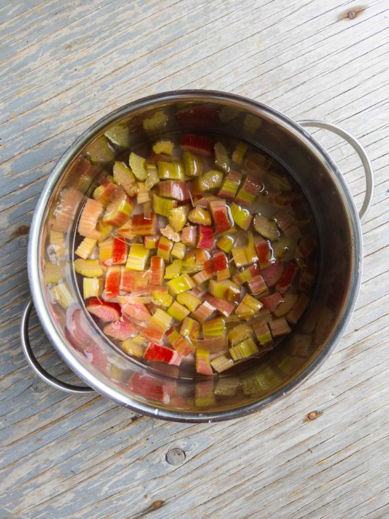 Chopped rhubarb with sugar and spices in a pot on a rustic background