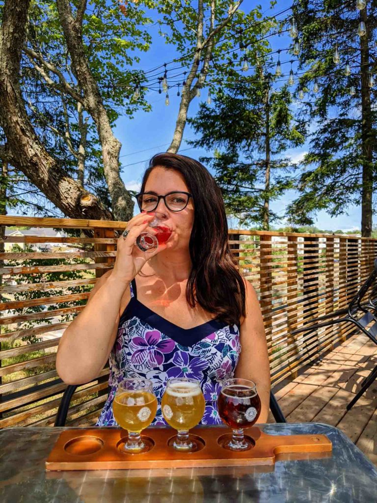 Ayngelina holding glass of beer from flight of beer on outside patio at Copper Bottom Brewing.