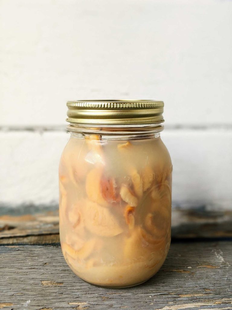 Mason jar of bottled bar clams on a rustic table with a white background.