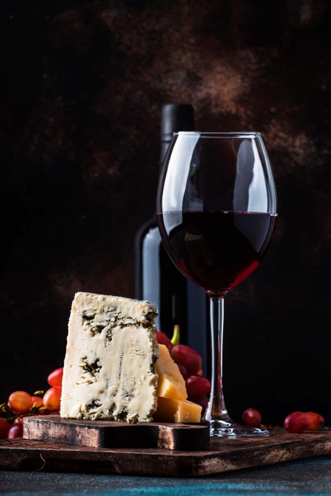 glass of port wine next to cheese fruit and nuts
