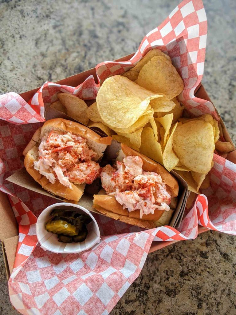 Lobster Shack Souris PEI lobster roll with chips and pickles on a table