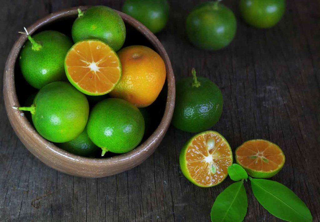 Calamansi or Philippine limes in a bowl and cut open on a wooden table