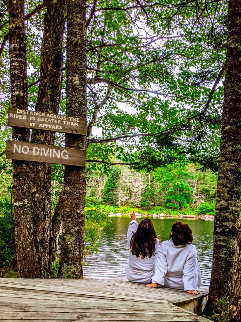 Two women sitting on dock in autumn at Trout Point Lodge in bathrobes