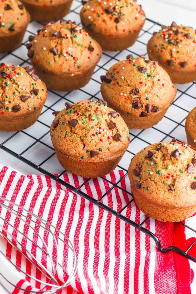Holiday muffins with sprinkles on a cooling rack with whisk and red and white tea towel.