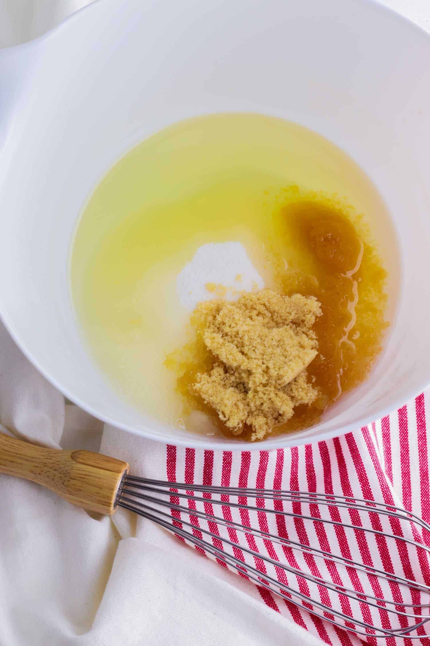 Butter, sugar and egg in a white bowl with whisk and red and white towel.