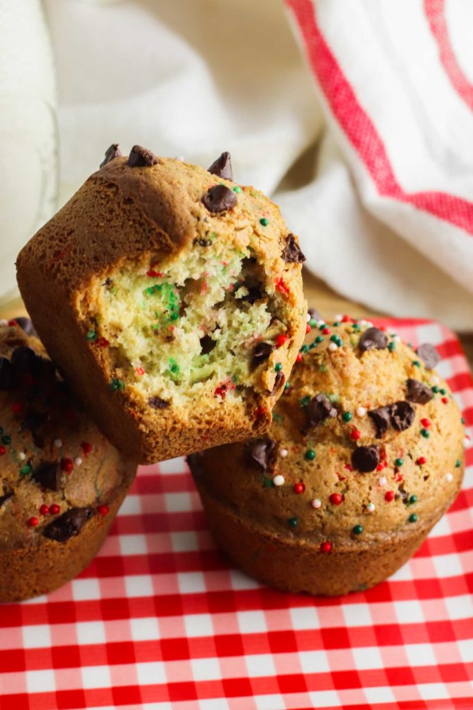 Christmas muffins stacked on red and white tablecloth with a bite out of one.