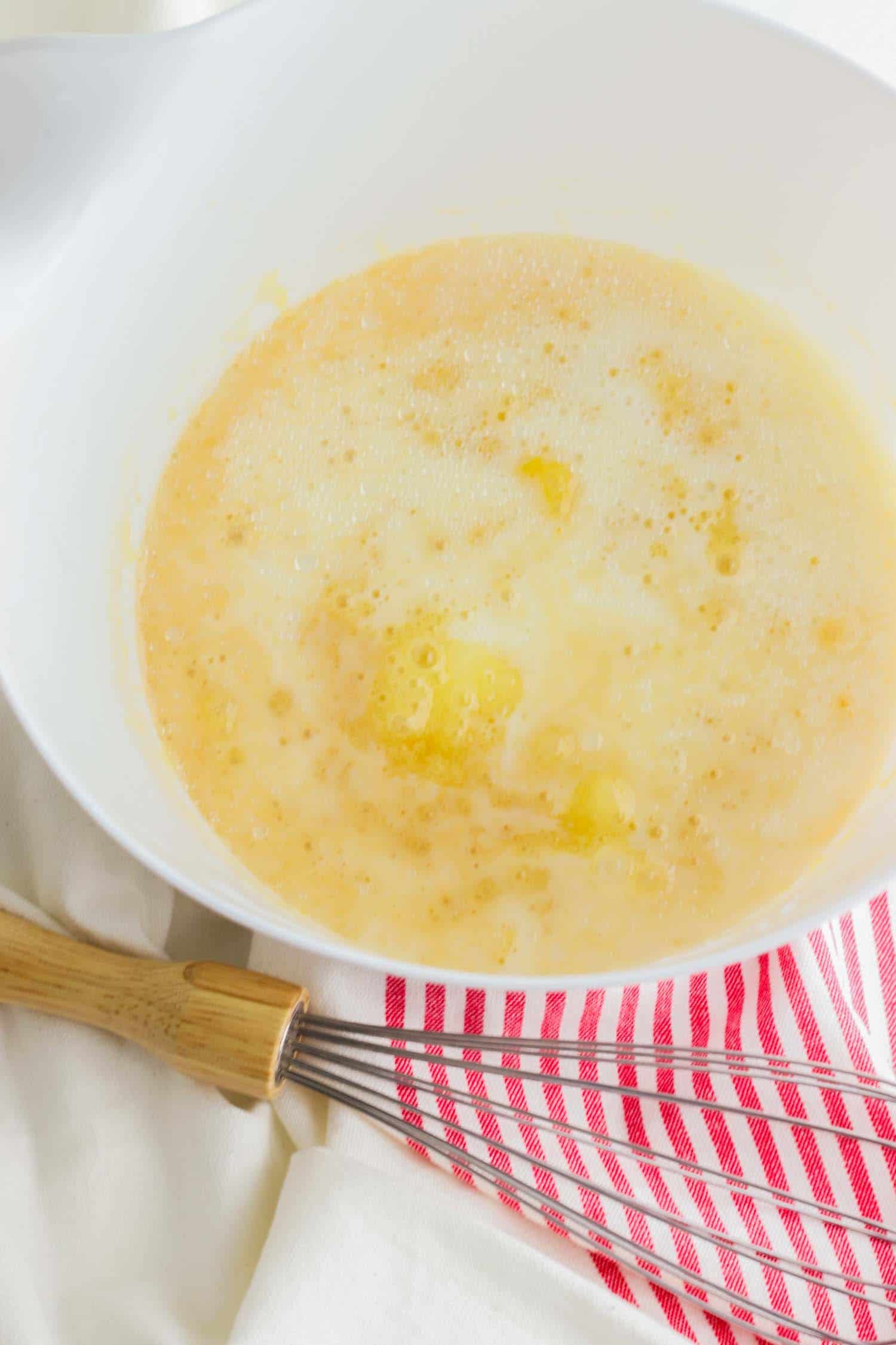 Egg, flour and butter in a white bowl with whisky and red and white towel.