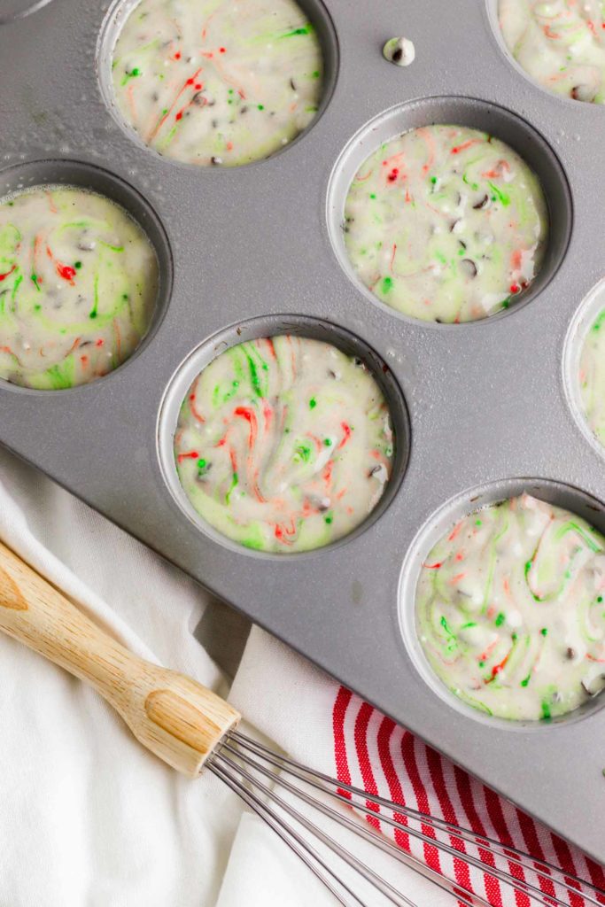 Christmas muffin batter in tins with whisk and red and white tea towel.
