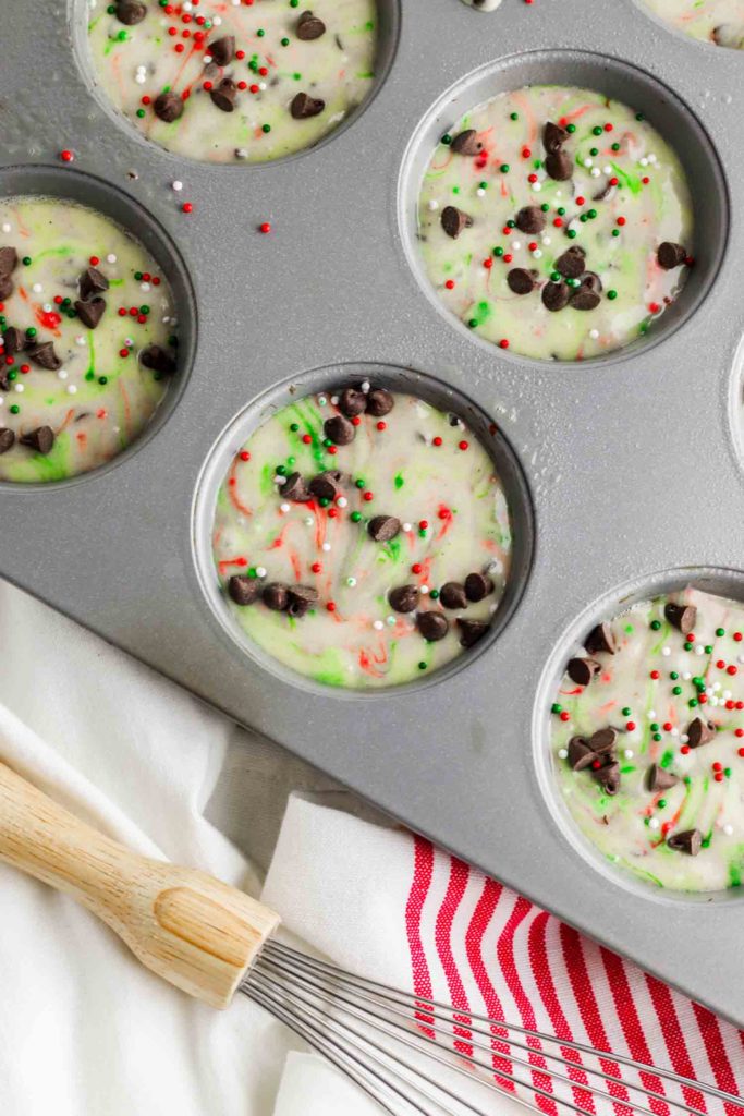 Christmas muffin batter in tins with whisk and red and white tea towel.