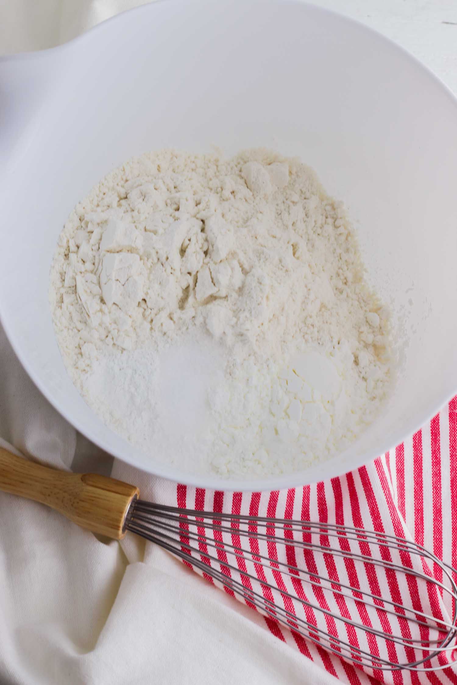 flour in a white bowl with whisk and red and white tea towel