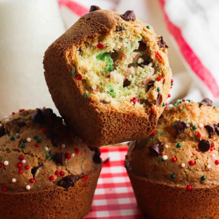 Christmas muffins stacked on red and white tablecloth with a bite out of one.