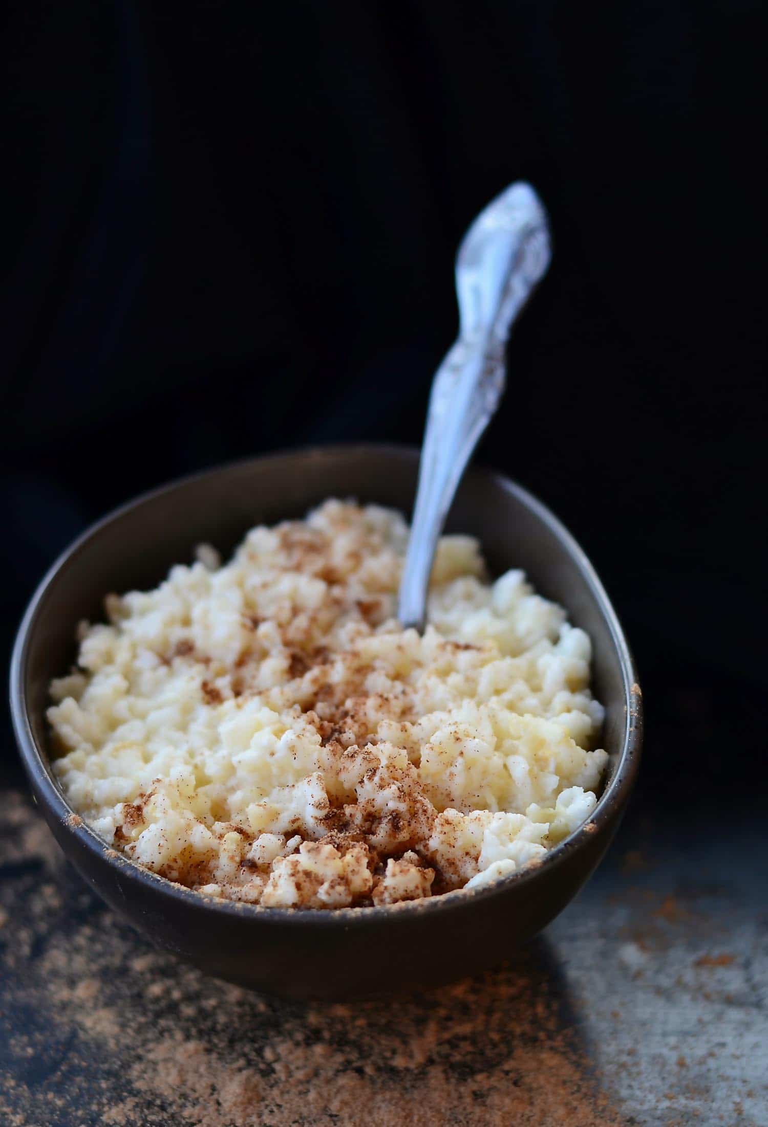 Rice pudding or arroz en leche in Guatemala in a brown bowl with a spoon on a dark background
