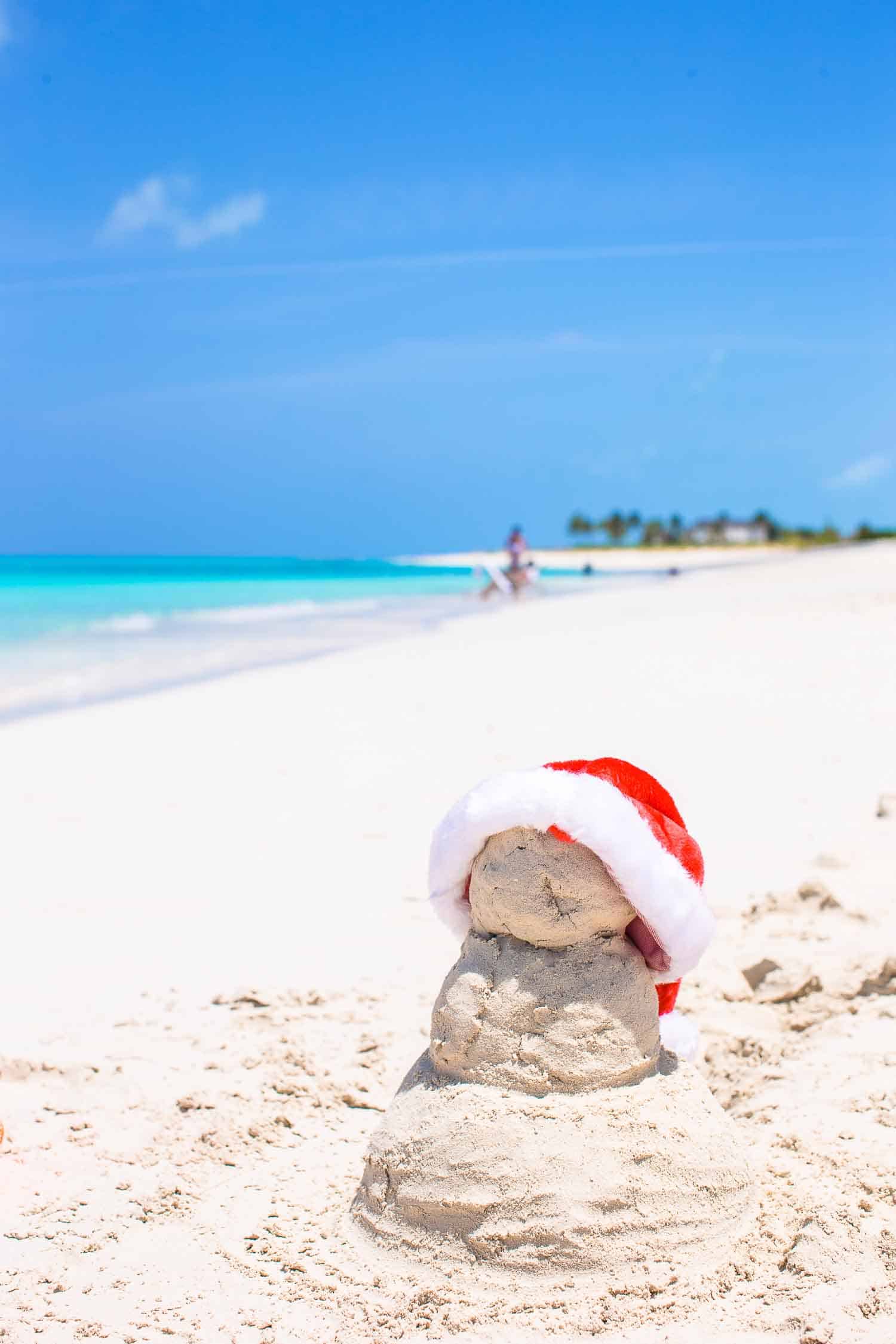 Little sandy snowman with red Santa Hat on white beach