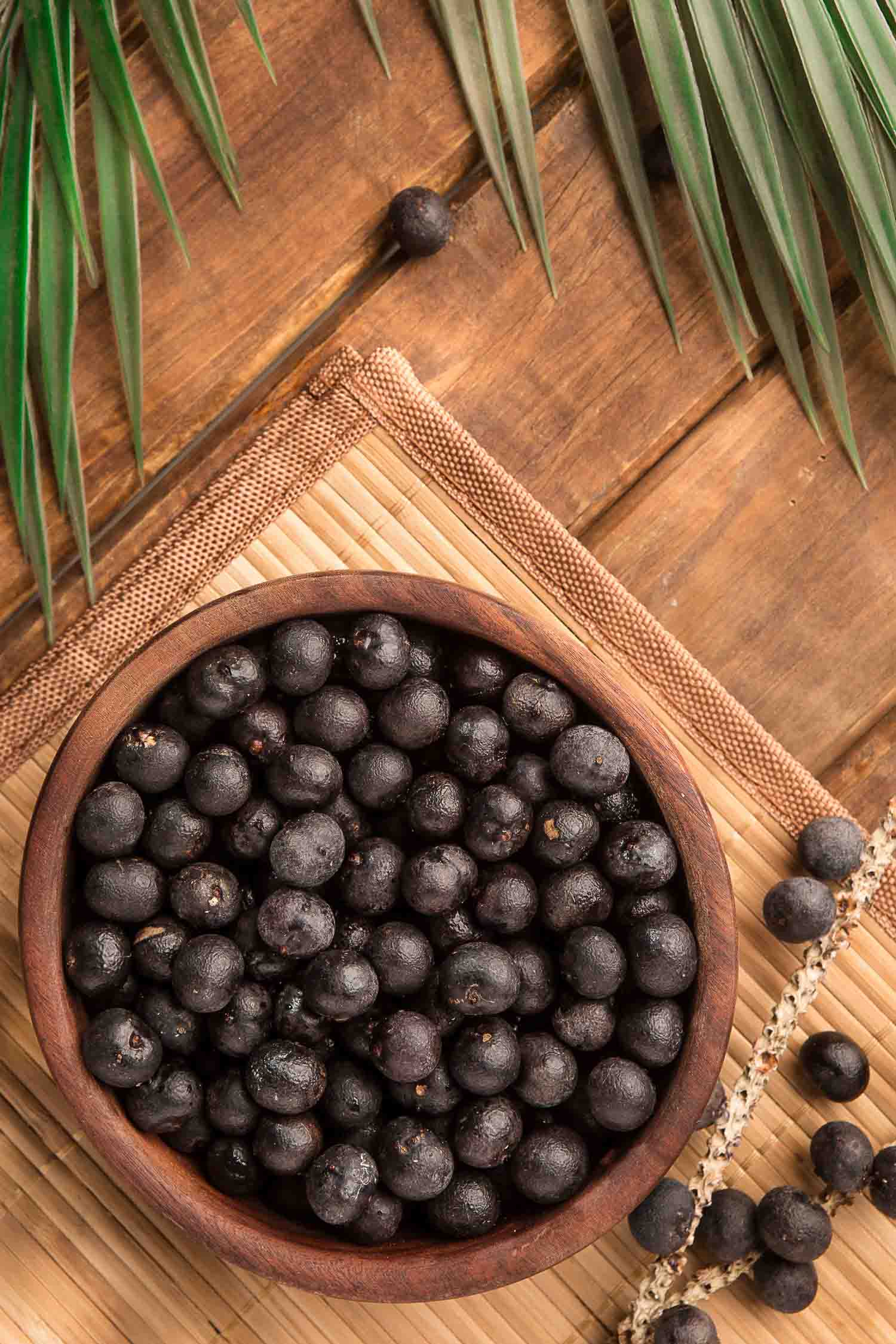 Brazilian fruits Acai berries in a bowl on a bamboo table with a palm leaf