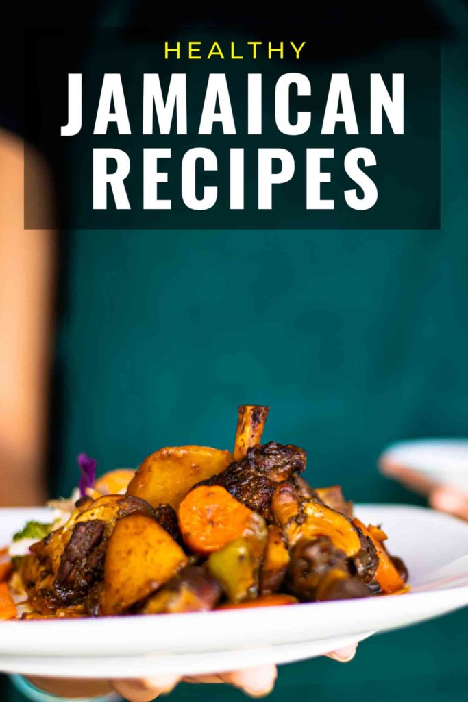 Person with green apron out of focus holding plate of healthy Jamaican food.