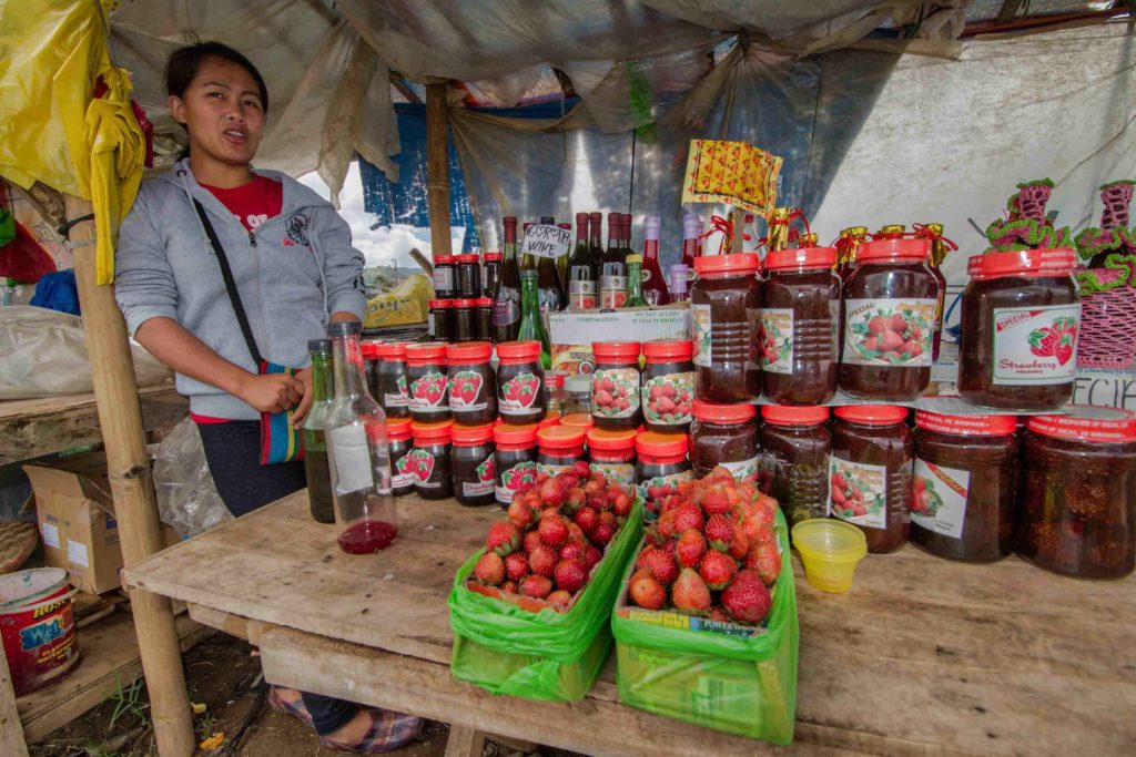 Market stand selling strawberry wine with vendor and strawberries on a table