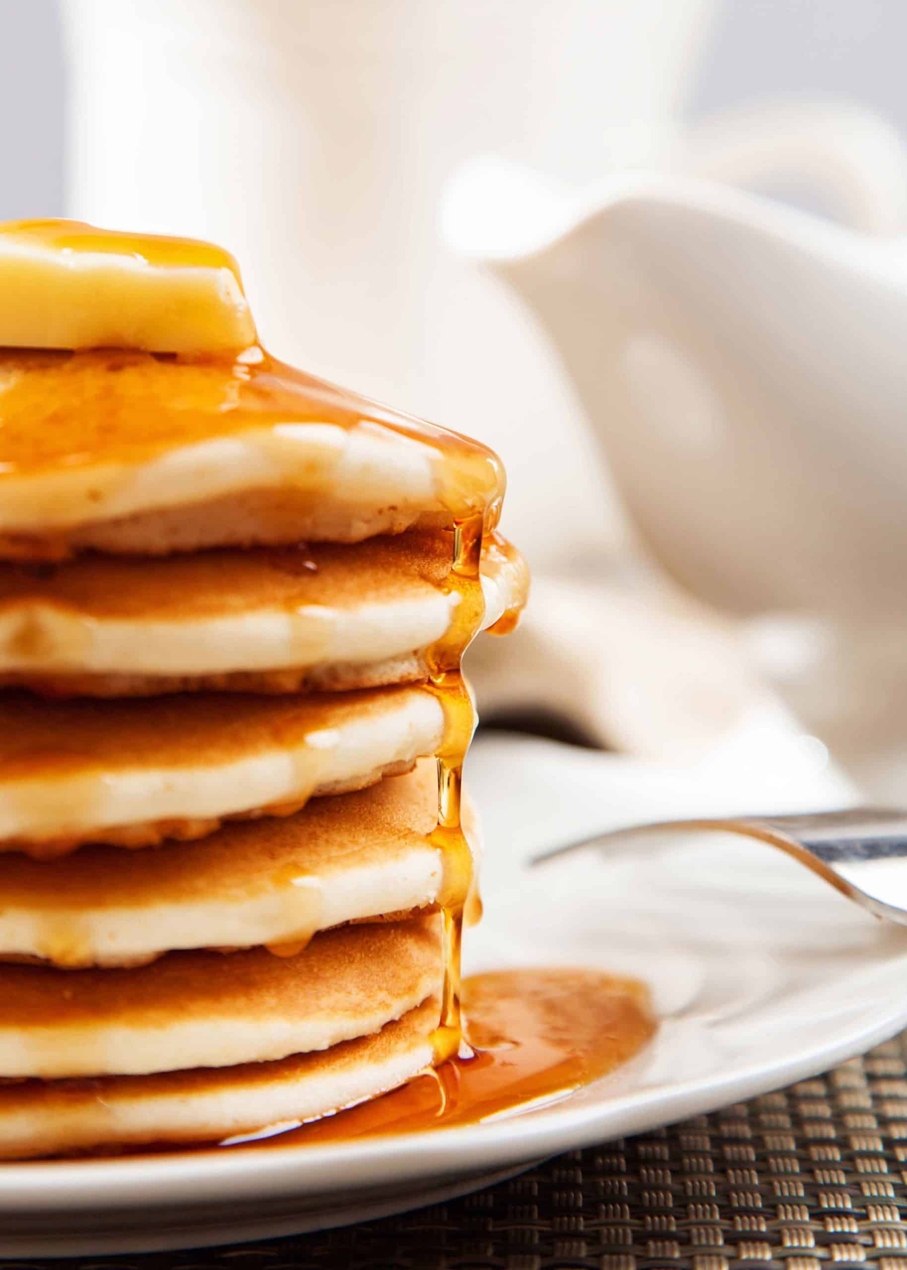 Cropped view of tall stack of dollar pancakes with maple syrup dripping