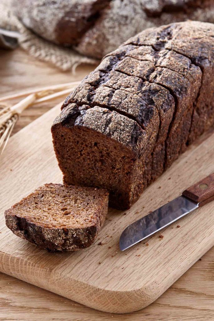 Sliced black rye bread with wheat and rye ears on a wooden table