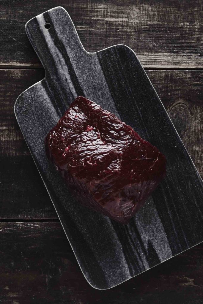 Top view of luxury raw piece of whale meat steak on black marble stone cutting desk and aged vintage wooden table