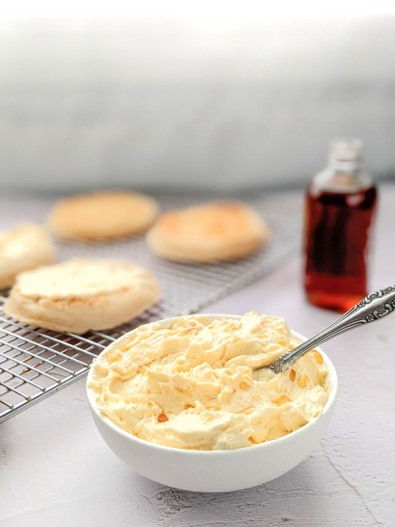 Whipped butter flavoured with maple in a small white bowl on a white table with crumpets in the background.