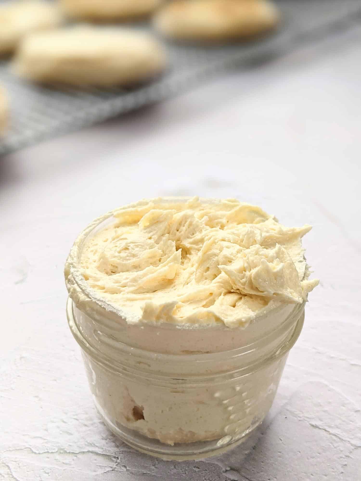 Maple brown butter in a small mason jar on a white table with crumpets in the background.