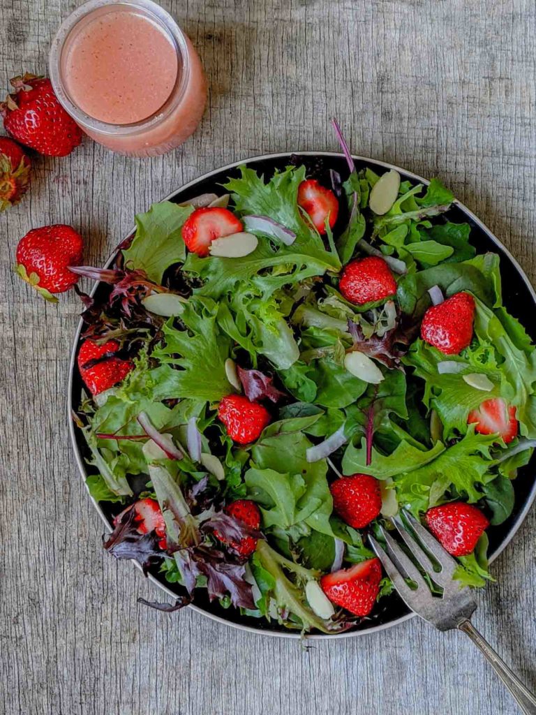 Strawberry salad with spinach, spring mix, arugula, red onion, slivered almonds on a black plate and rustic surface.