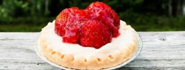 Individual strawberry tart on a wooden rail with trees in background.