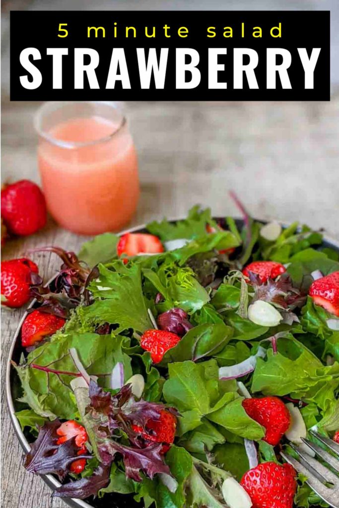 Strawberry salad with spinach, spring mix, arugula, red onion, slivered almonds on a black plate and rustic surface.