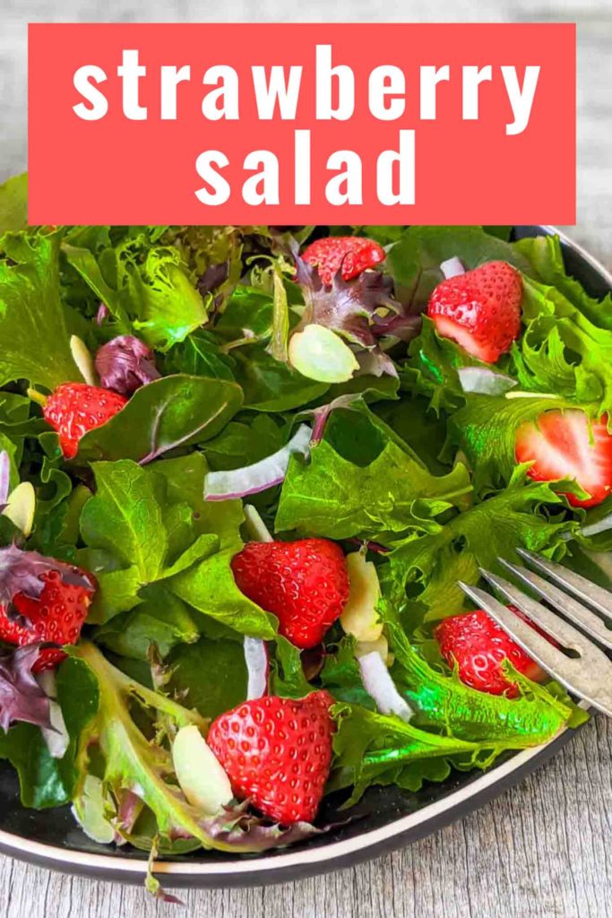 Strawberry salad with spinach, spring mix, arugula, red onion, slivered almonds on a black plate and rustic surface.