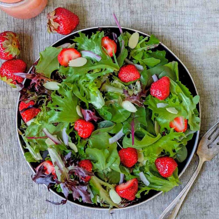 Strawberry salad with spinach, spring mix, arugula, red onion, slivered almonds on a black plate and rustic surface.